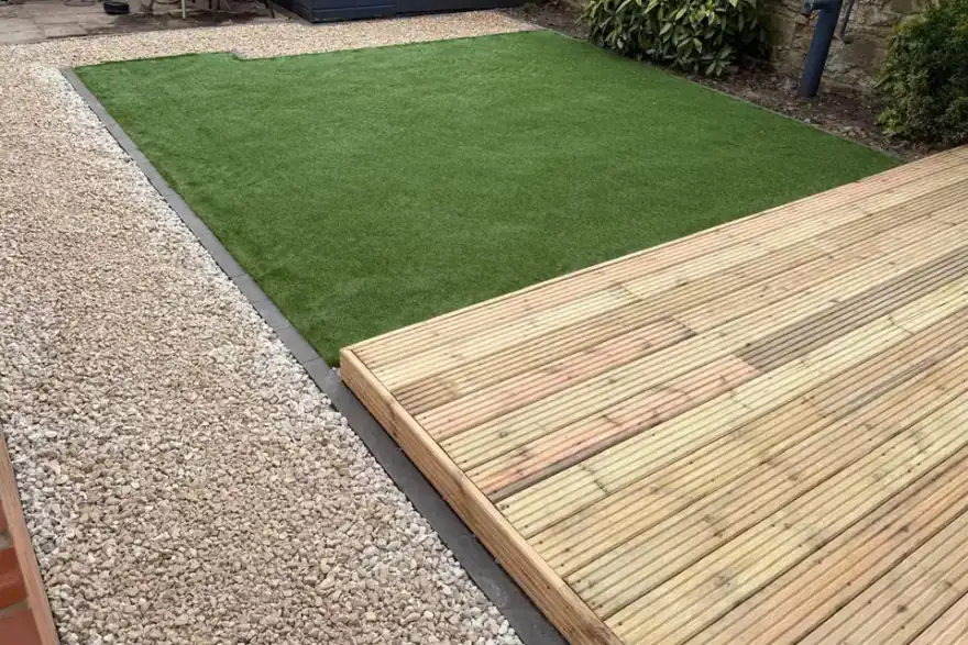 Backyard with wood deck, artificial grass lawn, gravel path, and a blue shed near brick walls.