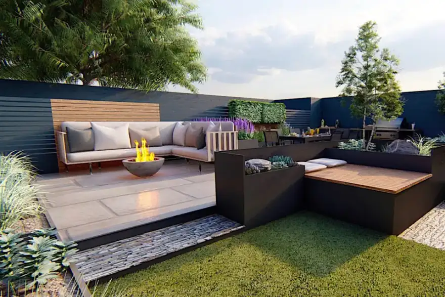 A modern outdoor patio with a beige sectional sofa, a fire pit, and a black dining table with chairs. The patio is surrounded by a dark fence, greenery, and tall trees, with a partly cloudy sky overhead.