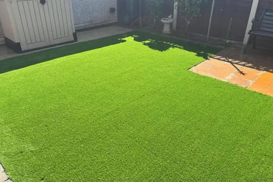 Backyard with bright artificial grass, storage shed, and patio stones in sunlight