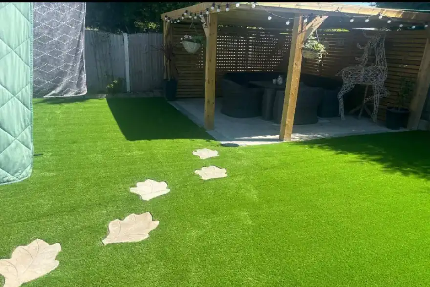 Backyard patio with green artificial grass and stepping stones leading to a shaded seating area.