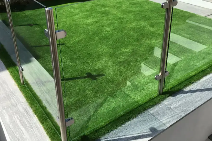 A small, fenced area of vibrant green artificial grass bordered by sleek glass panels