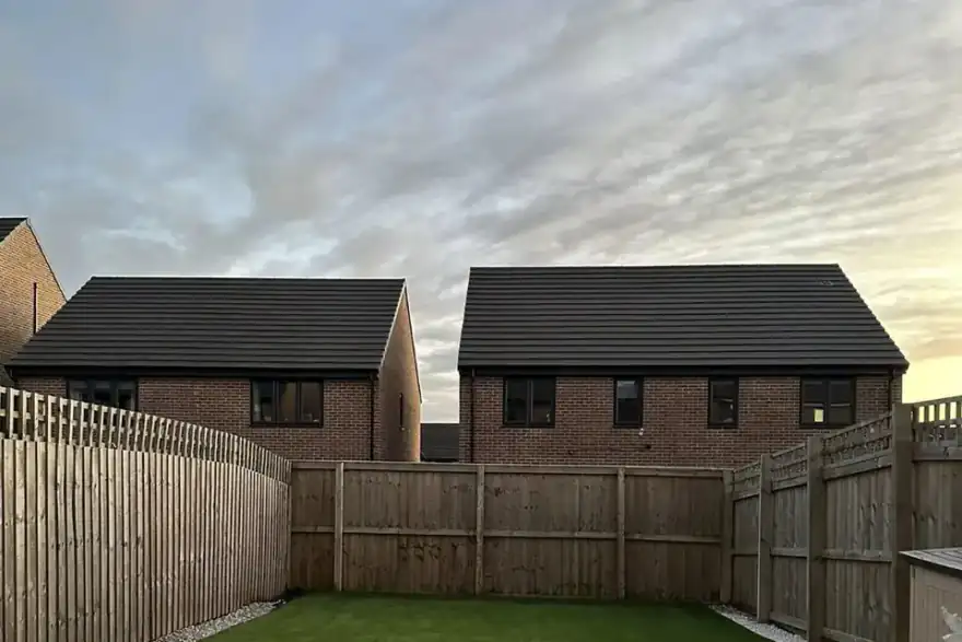 Artificial grass lawn with gravel margins in a new build garden at sunset