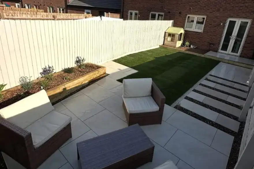 Porcelain patio with rattan furniture, stepping stones across a lawn and a sleeper raised bed