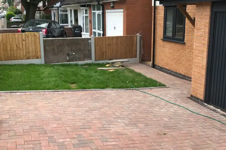 Red block paved driveway with a garden and fence