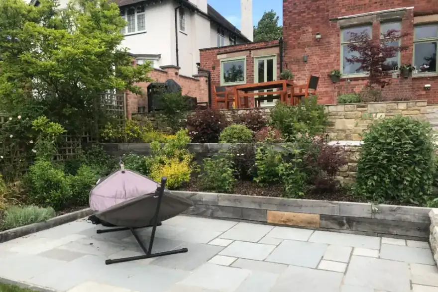small stone patio with hammock and railway sleeper walling for flower beds