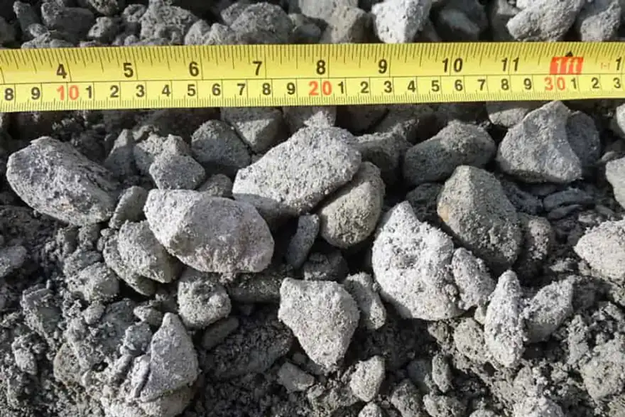 A close-up of a pile of grayish Type 1 Crushed Granite - Bagged stones, varying from small to medium sizes, with a yellow measuring tape above them. The rough textures and uneven shapes are perfect for your next project.
