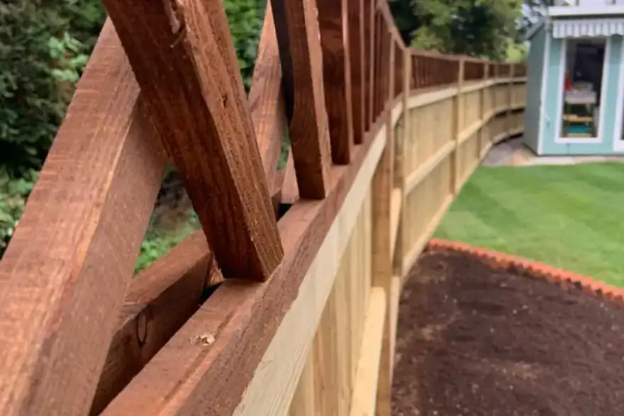 New wooden fence with brown trim and a garden shed in the background.