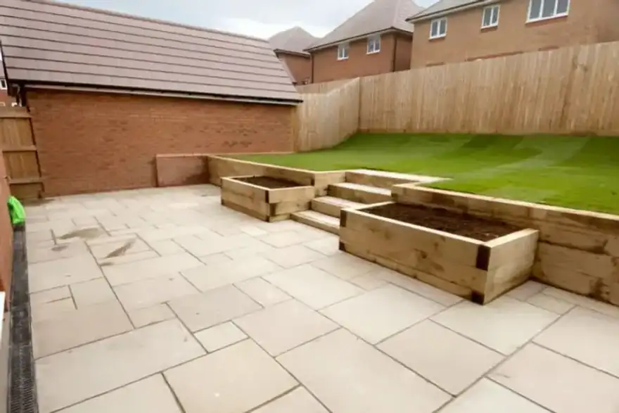 Back garden patio with large wooden planters, stone paving, and grassy lawn