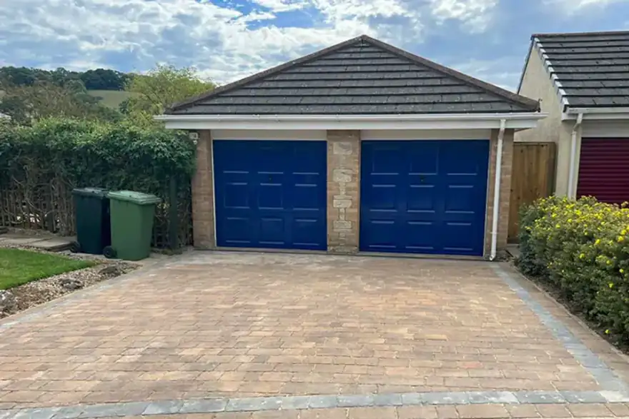 A brick driveway with two blue garage doors.