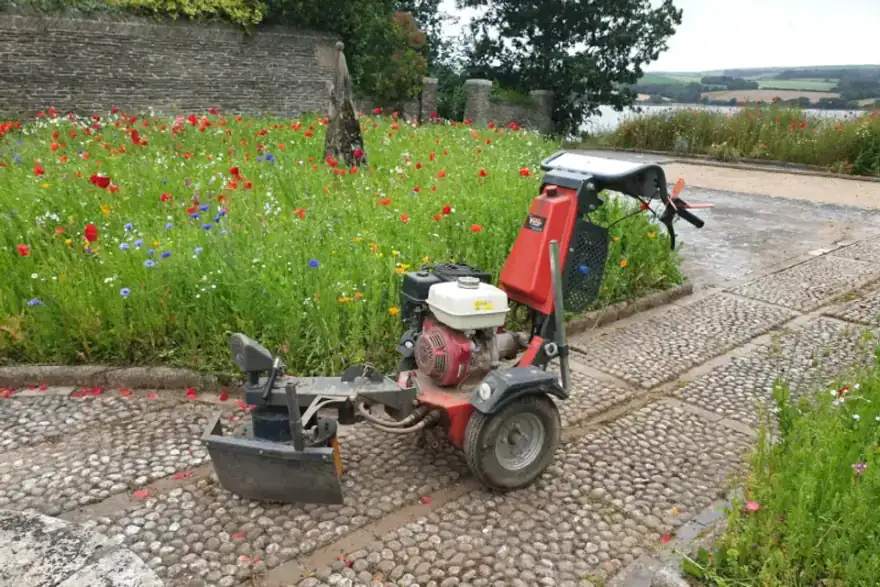 Trelawny chemical-free weed control machine on a cobbled path beside a wildflower border in Cornwall