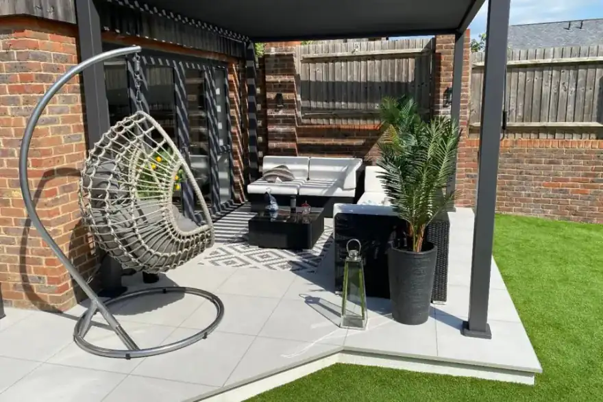 An outdoor seating area with a hanging chair etc on paving next to artificial grass